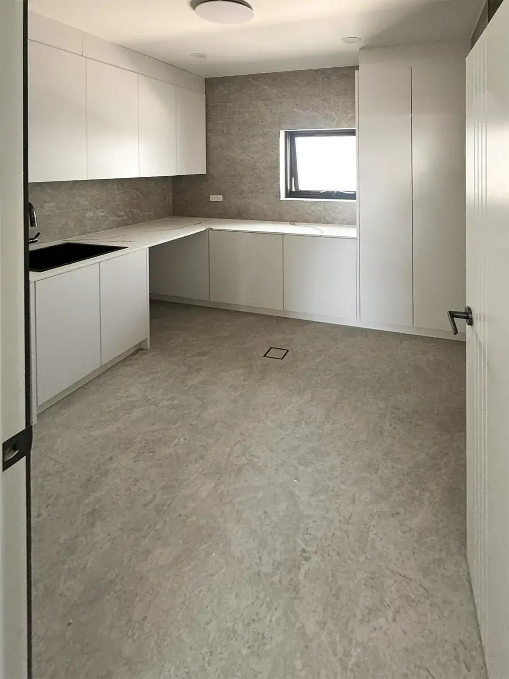 Modern laundry with white handleless cabinetry, stone benchtop and grey stone-look tiled floor